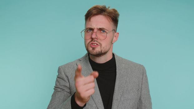 Quarrel. Displeased business man gesturing hands with irritation and displeasure, blaming scolding for failure, asking why this happened. Young adult guy isolated alone on blue studio wall background