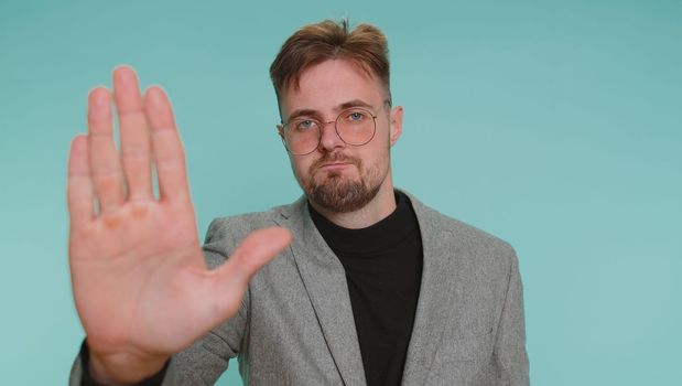 No stop, enought. Business man say No, hold palm folded crossed hands in stop danger gesture, warning of finish, prohibited access, declining communication, body language. Young guy on blue background