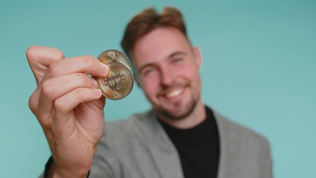 Business man winner showing golden BTC bitcoins. Career wealth, cryptocurrency investment, mining future technology. Young adult guy fooling making faces. Happy businessman isolated on blue background