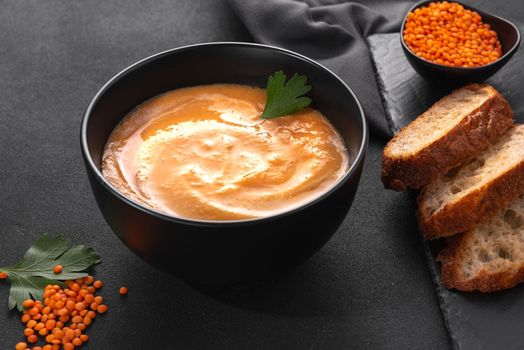 Lentil soup with red lentils whipped into a puree with cream on a dark background top view.