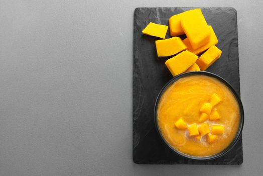 Pumpkin traditional soup with creamy silky texture. Vegetarian fall pumpkin puree soup in a black bowl . Pumpkin soup. Empty space for text and recipe.