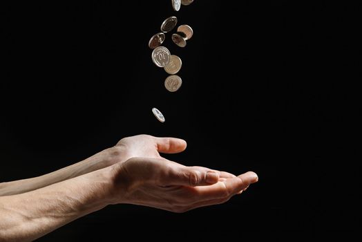 Coins fall into the hands of a poor man. Financial aid on dark background whit copy space
