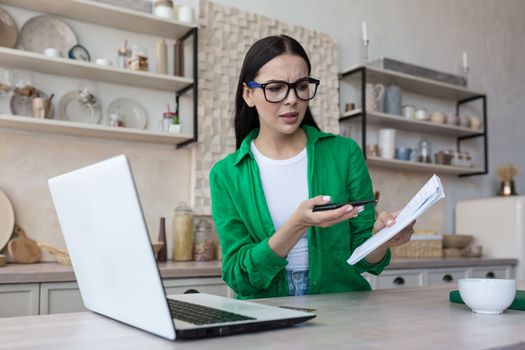 Online business meeting. Young upset woman talking on video call from laptop with tax, bank, creditor. Quarrels, shows a notebook with bills.