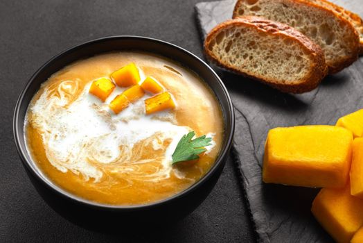Pumpkin traditional soup with creamy silky texture. Bread and ingredients for the soup next to each other.