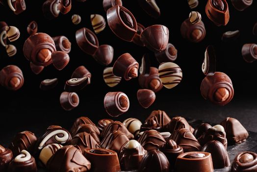 chocolate candies with various fillings, sweet food background. Levitation or flight of sweet brown chocolates or confit on a dark black background.