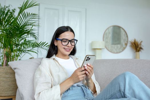 Happy and smiling young teenage girl lying on sofa at home and using phone. Receives messages, chats with friends, boyfriend, chat news, blogs, social networks, online shopping..