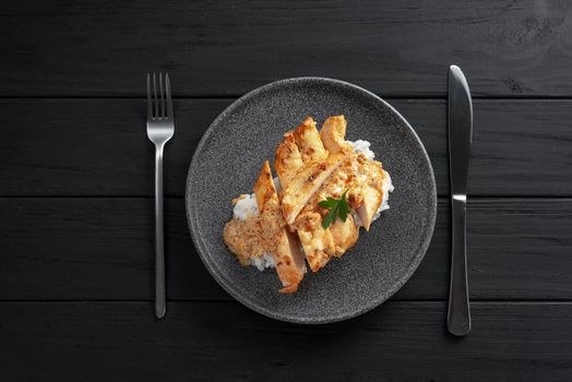 Chicken breast in cream sauce with rice top view. Plate with chicken breast on dark wooden background. Top view.