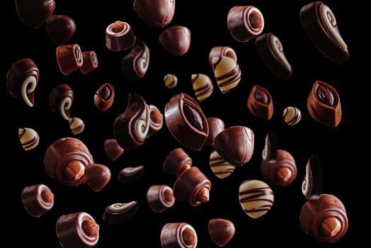 Levitation or flight of sweet brown chocolates or confit on a dark black background
