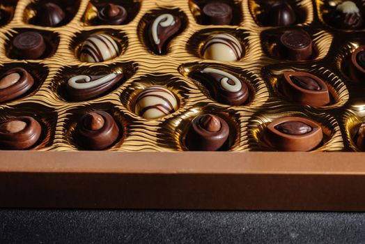 A box of different chocolates. Chocolate assortment mix on the black table, top view.