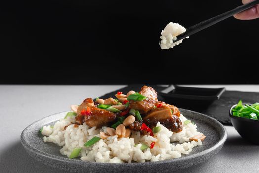 Asian cuisine. A woman's hand holds Asian food sticks. Rice with chicken on a gray background view from above. Boiled rice with stir-fried sliced chicken breast and basil.Thai cuisine.
