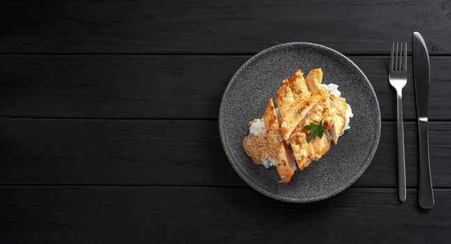 chicken breast with rice on a black wooden background. Blank space for text top view.