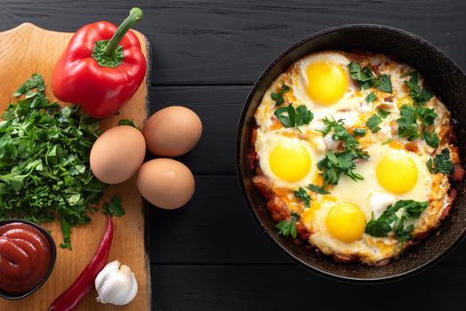 Shakshuka in an iron skillet with ingredients. Middle Eastern traditional dish. Fried eggs with tomatoes, bell peppers, vegetables and herbs, scrambled eggs