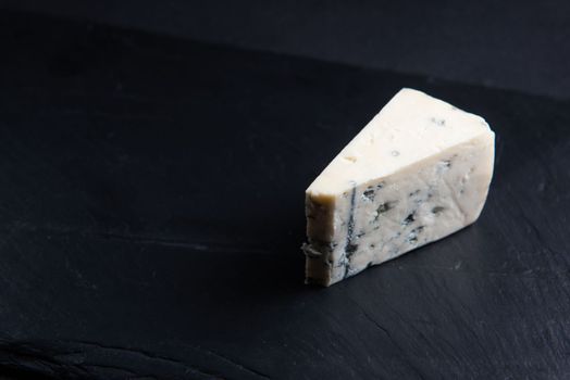Blue cheese, dor blue or roquefort mold cheese slice on cutting board with basil leaves, lifestyle food