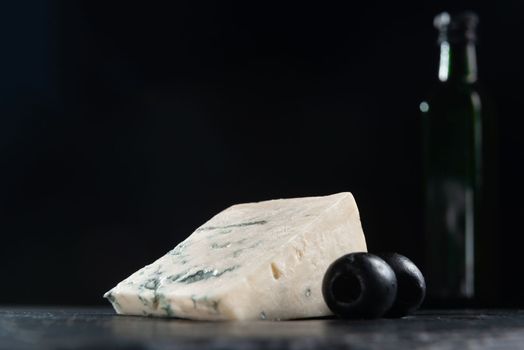 French cheese, roquefort with olives on plate, closeup. French Roquefort cheese with olives on a dark background. Moldy cheese with olives. Blue cheese on black background.