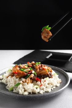 Asian cuisine. A woman's hand holds Asian food sticks. Rice with chicken on a gray background view from above. Boiled rice with stir-fried sliced chicken breast and basil.Thai cuisine.