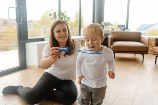 mother and son playing with soap bubbles. The child blows on the bubbles, but he doesn't succeed. A happy childhood and a healthy family, happy family relationships
