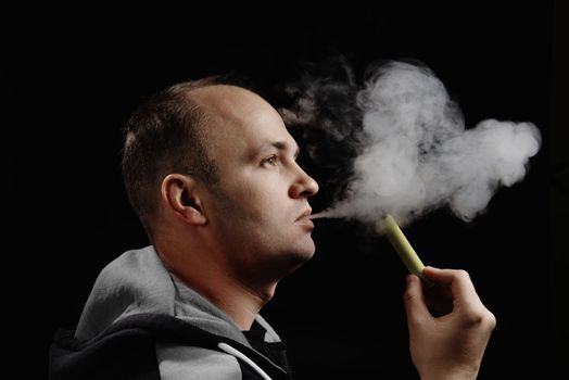 A man uses an electronic cigarette against a black background. Space for text. Alternative to smoking. How to quit smoking