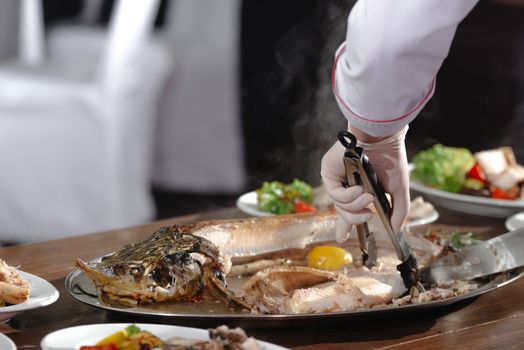 A hand with a knife cuts the fish. Bistro chef preparing lunch. A chef is cutting up a sturgeon. cooked fish in a professional kitchen. Chef cuts sturgeon fish.