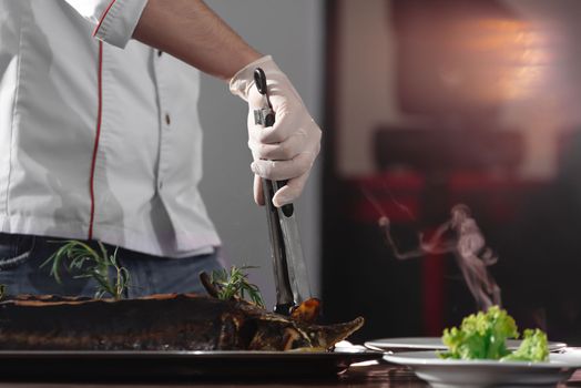 A hand with a knife cuts the fish. Bistro chef preparing lunch. A chef is cutting up a sturgeon