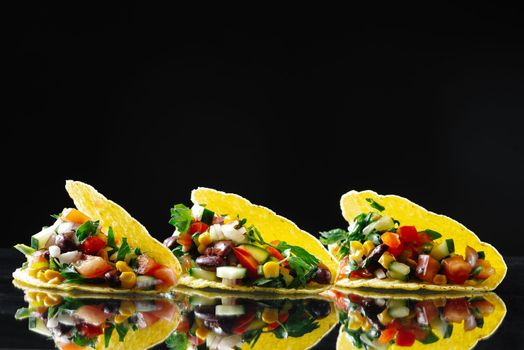 3 vegetarian tacos on a black glass background