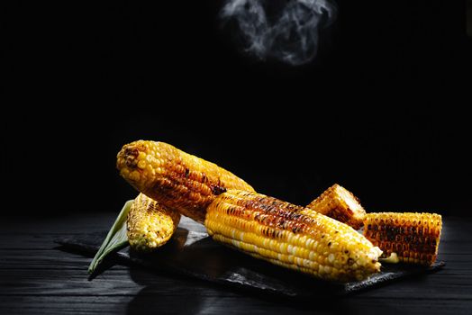 Grilled corn with smoke. A cob of corn roasted over charcoal on a wooden board. Whole corn cobs