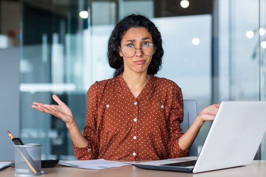 Frustrated and tired business woman looking at camera, Hispanic woman unhappy with work result, working inside office using laptop at work.