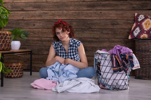 Attractive girl sorts clothes for washing. Short curly hair. Metal basket full of clothes prepared for washing. A wall of brown boards.