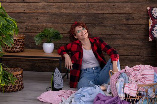 Happy and smiling girl that she will be able to quickly iron clean clothes after washing. Full of vigor and strength to work. A wall in the house made of boards.