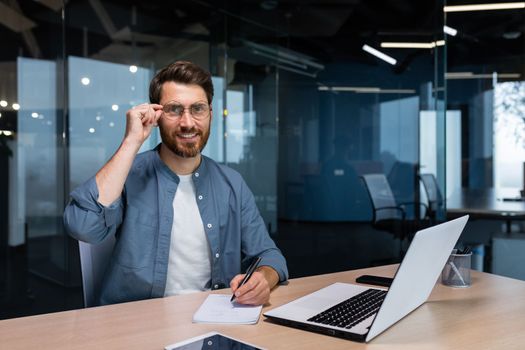 Portrait of successful businessman behind paper work, man in shirt smiling and looking at camera, financier boss inside office using laptop in work at workplace.