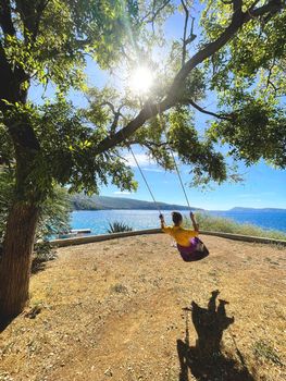 happy lady rides on a swing tied to a tree behold the beautiful summer landscape of the sea and islands.