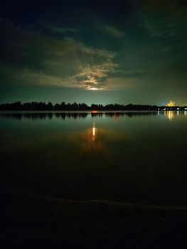 photography of evening nature by the river. Rising full moon above the trees. Beautiful reflection of the moon path in the water.
