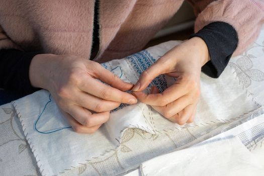 Close-up of a woman's hands sewing a Ukrainian national embroidered shirt.