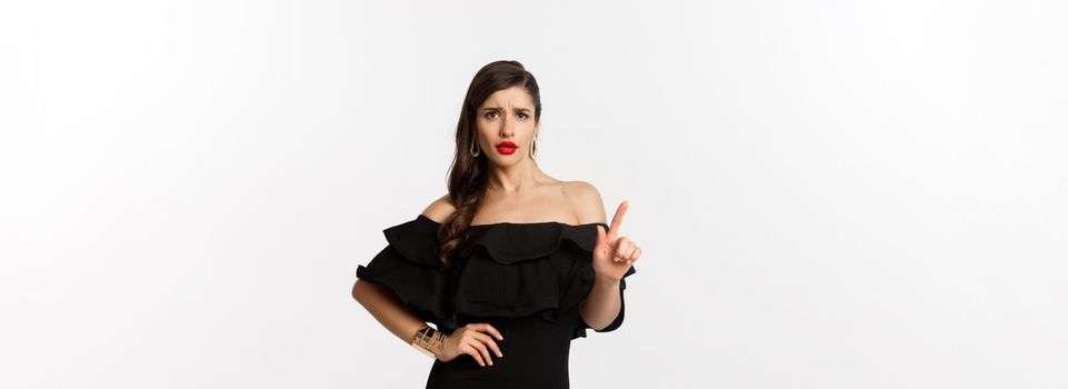 Fashion and beauty. Sassy woman in black dress saying no, disagree and shaking finger displeased, rejecting offer, declining something, standing over white background.