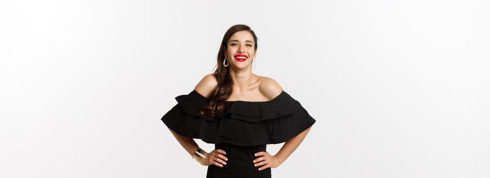 Beauty and fashion concept. Elegant young woman wearing party dress and red lipstick, laughing at camera, standing cheerful against white background.