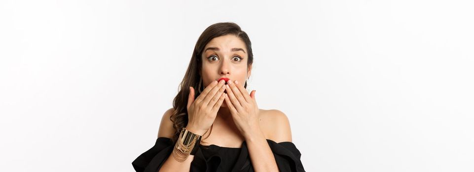 Fashion and beauty concept. Close-up of excited young woman looking amazed, cover mouth with hands and staring at camera with rejoice, white background.