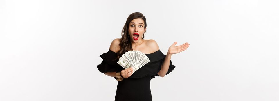 Beauty and shopping concept. Excited lucky woman winning money, looking amazed and holding dollars, standing over white background.