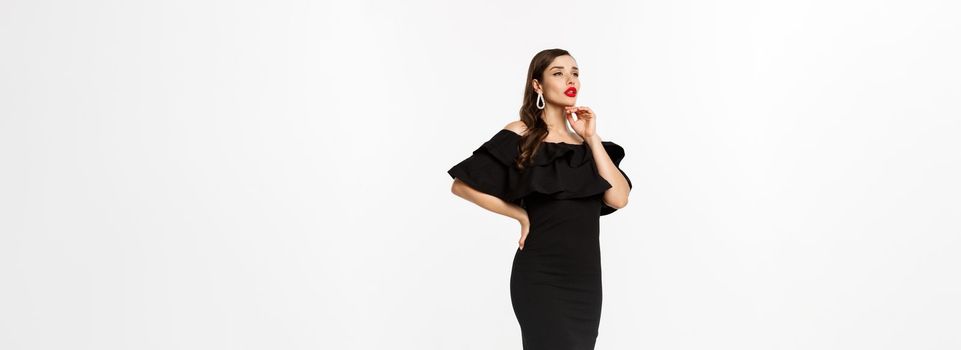 Vertical view of beautiful young woman in luxurious dress, red lips and jewelry, standing with christmas gifts on white background, standing over white background.