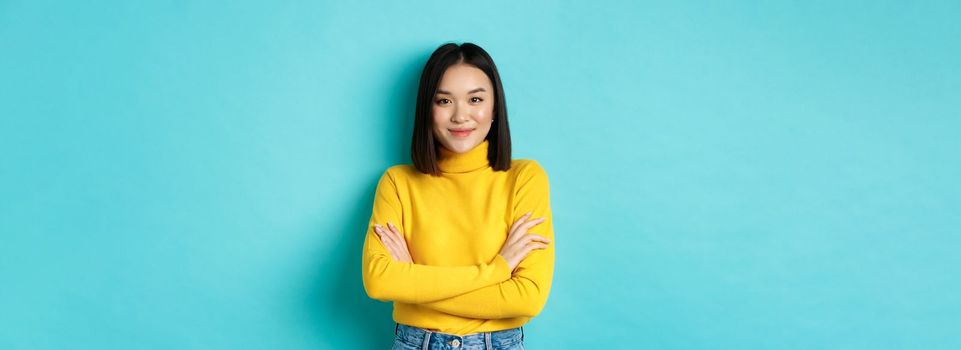 Attractive asian woman with short dark hair, cross arms on chest and smiling confident, standing over blue background.