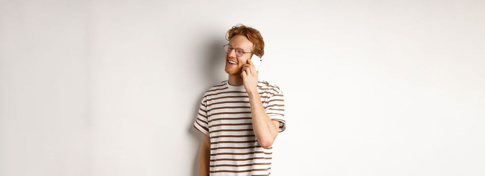 Profile of happy young handsome man talking on mobile phone, looking left and smiling, standing over white background.