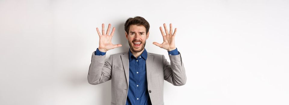 Frustrated man giving up, raising hands up in surrender and screaming, having argument, wearing suit and looking distressed, white background.