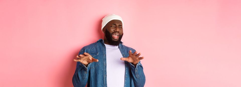 Image of disgusted picky Black man cringe from something disturbing, refusing bad offer, grimacing with dislike and aversion, standing over pink background.