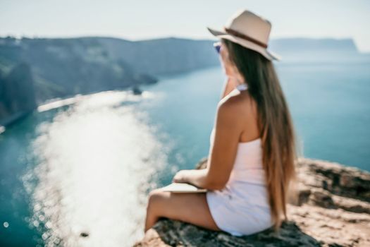 Successful business woman in yellow hat working on laptop by the sea. Pretty lady typing on computer at summer day outdoors. Freelance, travel and holidays concept.