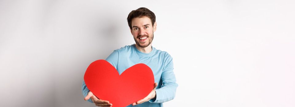 Happy gay man giving big red heart to his lover on valentines day, concept of romantic date and love celebration, standing over white background.