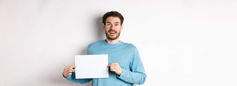 Romantic man looking with hopeful face at camera, showing sign card, blank piece of paper for banner or logo, standing over white background.