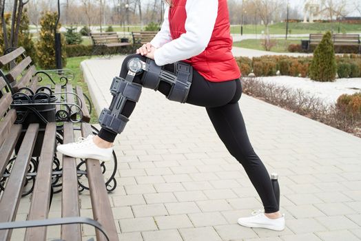 Woman wearing sport clothes and knee brace or orthosis after leg surgery, walking down the stairs in the park. Medical and healthcare concept.