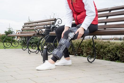 Woman wearing sport clothes and knee brace or orthosis after leg surgery, walking in the park. Medical and healthcare concept.