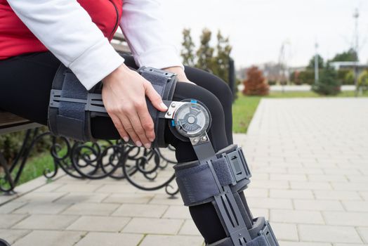 Woman wearing sport clothes and knee brace or orthosis after leg surgery, walking in the park. Medical and healthcare concept.