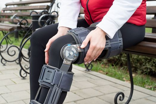 Woman wearing sport clothes and knee brace or orthosis after leg surgery, walking down the stairs in the park. Medical and healthcare concept.