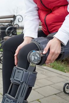 Woman wearing sport clothes and knee brace or orthosis after leg surgery, walking in the park. Medical and healthcare concept.