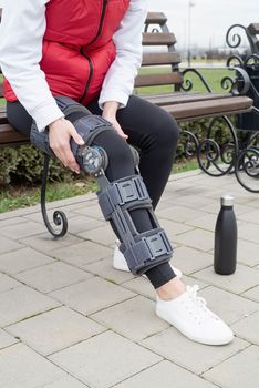 Woman wearing sport clothes and knee brace or orthosis after leg surgery, walking down the stairs in the park. Medical and healthcare concept.